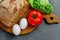 Eggs, tomato, lettuce leaves, bread. Wooden board with Ingredients for cooking. From above