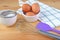 Eggs, whisk and kitchen utensils on wooden background