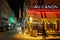 Eiffel tower illuminated at night and street with people and typical restaurant in Paris, France