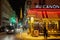 Eiffel tower illuminated at night and street with people and typical restaurant in Paris, France