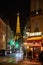 Eiffel tower illuminated at night and street with people and typical restaurant sign in Paris, France
