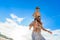 Eight years old boy sitting on dad`s shoulders. Both in swimming shorts and sunglasses, having fun on the beach. Bottom view