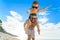 Eight years old boy sitting on dad`s shoulders. Both in swimming shorts and sunglasses, having fun on the beach. Bottom view