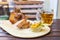 Eisbein with bread, vegetables and beer on wooden cutting board