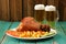 Eisbein with french fries, vegetables and two mugs of beer on wooden background