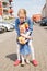 Elder blond hair girl hugs her younger sister outdoor near tenements houses in a sunny summer day