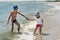 The elder brother plays on the beach with his younger brother, waves, happy children