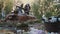 Elder couple filling bottles from rusty pipe wellspring in woods full of trash