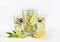 Elder flowers  lemonade with lemon slices in glasses and jug with branch and blooming at white background. Healthy seasonal drink