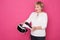 Elderly in 60s woman plays in VR helmet. She stands in white blouse on pink background and looks happy