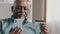Elderly African Dominican old mature man at home online transaction buying hold smartphone credit card successful