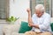 An elderly Asian man sits with arm pain on the sofa in his house.