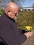 Elderly bald man is standing in the garden with a yellow primula in a plastic flower pot in his hands. Yellow Primrose