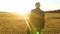 An elderly businesman in serious suit with briefcase in hand walks along road in evening in glare of setting sun