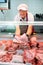 Elderly butcher shop seller laying out raw pork ribs in display case