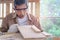 Elderly carpenter wearing safety glasses goggles blowing sawdust off piece of wood plank, senior craftsman working at wooden desk