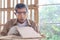 Elderly carpenter wearing safety glasses goggles blowing sawdust off piece of wood plank, senior craftsman working at wooden desk