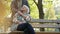 An elderly caucasian grey-haired woman sitting on a bench in a park and touching her husband\'s hand.