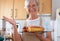 Elderly Caucasian woman in the home kitchen proudly displays a freshly baked homemade plumcake served with berries. Cooking at