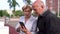 An elderly couple looks and laughs at a funny picture on the Internet on their smartphone walking in the open air.