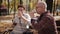 Elderly couple on a Park bench drinking coffee or tea from a Cup, eating croissants and nice talk.