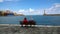 An elderly couple sitting on a bench on the promenade and admire the views in the center of Chania