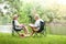 Elderly couple Sitting on a black chair in a shady garden And there is a picnic basket for bread and fruit.