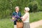 An elderly couple walks through the forest and a man gives a woman a woven basket with a bouquet of flowers of purple lupines