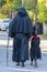 An elderly dad and his little daughter dressed as a monk and a witch for Halloween are walking down the street, rear view.