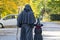 An elderly dad and his little daughter dressed as a monk and a witch for Halloween are walking down the street, rear view.