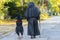 An elderly dad and his little daughter dressed as a monk and a witch for Halloween are walking down the street, rear view.