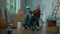 An elderly disabled man in a wheelchair examines a bucket of paint. A pensioner plans repairs and wall decoration. Room