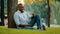 Elderly ethnic man African American smiling friendly entrepreneur sitting on grass in city park businessman with