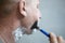 An elderly European man with foam on his face is shaving with a machine. Life of real people