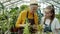 Elderly farmer doing inventory in greenhouse when girl bringing pot plant talking