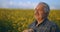 An elderly farmer in a hat stands at sunset and looks into the distance. The concept of a successful working day