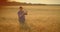 An elderly farmer man in a shirt and baseball cap stands in a field of cereal crops at sunset and looks at the spikes of