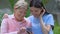 Elderly female showing family photos to young volunteer, nursing home park