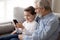 Elderly grandfather embraces grandson holding smartphone using gadget at home