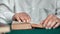 Elderly grandfather wrinkled hands reading book at library on desk closeup