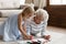 Elderly grandma teach little granddaughter drawing lying on warm floor