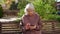 An elderly grandmother is sitting on a bench with a phone in her hands.