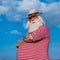 Elderly gray-haired man with a beard in a striped bathing suit and hat posing on the beach. Senior citizen on vacation