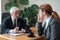 An elderly gray-haired man interviews a young red-haired woman. Male old boss hires a female employee. Discussion of two