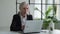 Elderly gray-haired woman uses a laptop comes up with an idea. Businesswoman working in a modern office.