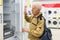 elderly grayhaired man pensioner looking refrigerator at counter in showroom of electrical appliance hypermarket