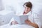 Elderly grey woman in white bathrobe sitting in hospital bed and reading book