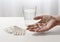 elderly hand of a senior is holding pills, water glass and blister pack on the white table, light background with copy space