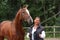 Elderly happy woman and brown horse in the forest