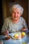 An elderly happy woman eating lunch sitting at the table.